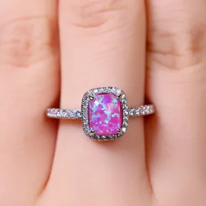 Vista macro di un anello rettangolare con opale rosa e halo di zirconi sulla mano