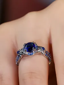 Macro shot of oval blue gemstone ring with intricate pavé diamonds on carved silver band