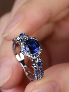 Detailed close-up of the silver ring featuring a round blue stone and side floral micro-pave