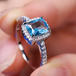 Macro view of white gold ring with rectangular blue gemstone and halo of side diamonds