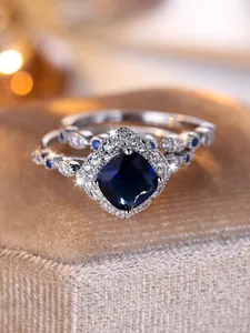 Macro view of cushion-cut blue gem and pavé diamond halo on silver wedding set