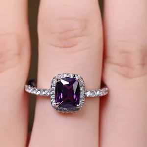 Close-up of a square cut purple gemstone ring with halo setting on a finger