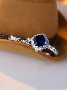 Macro shot of cushion cut blue sapphire ring with twisted band and diamond halo