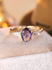 Dettaglio macro di un anello dorato con gemma ovale viola e due pietre laterali