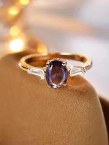 Dettaglio anello con gemma ovale viola e diamanti trapezoidali su supporto di velluto