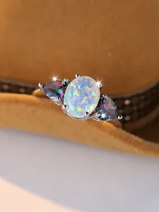 Macro shot of oval white opal ring with rainbow side stones and four-prong setting