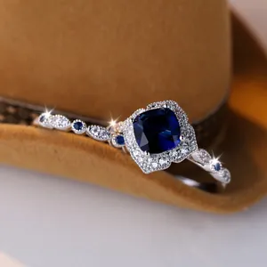 Luxurious silver ring with blue cushion cut stone and diamond halo on brown felt surface