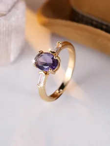 Dettaglio anello con gemma ovale viola e pietre baguette laterali su fascia dorata