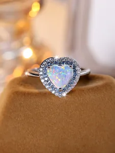 Détail macro d'une bague opale en cœur avec pavé de diamants bleus et blancs sur deux rangs