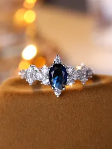 Dettaglio dell'anello con zaffiro blu ovale e scintillanti zirconi bianchi a lato