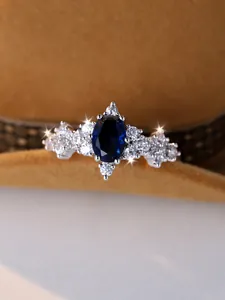 Dettaglio macro di un anello con zaffiro blu ovale e pietre laterali su metallo bianco