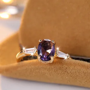 Elegante anello placcato oro con pietra viola ovale e diamanti laterali su sfondo morbido