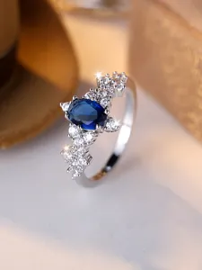 Dettaglio dell'anello con pietra blu ovale e cluster di diamanti su montatura d'argento