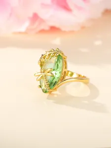 Detail of gold ring featuring a dragonfly, leaves, and a large faceted green gemstone