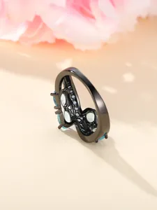 Macro view of black plated irregular ring featuring blue zircon accents on a floral background
