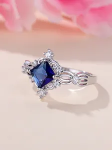 Dettaglio macro di anello con gemma blu quadrata e finitura traforata con zirconi bianchi