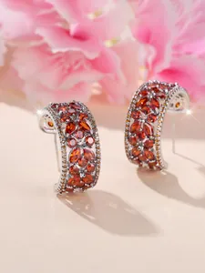 Détail des boucles d'oreilles C argentées avec zircone orange sur fond floral rose