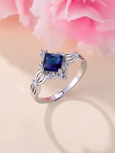 Macro di un anello con pietra blu quadrata e motivi traforati in argento con zirconi