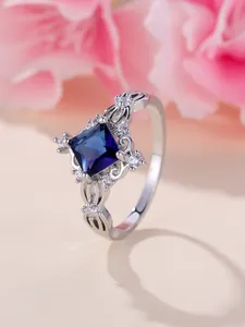Dettaglio anello con gemma blu quadrata, zirconi bianchi e fascia metallica traforata