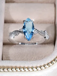 Macro shot of marquise-cut blue gemstone with twisted silver band and tiny diamonds