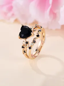 Macro detail of heart-shaped black gemstone set in vine-style golden dual rings