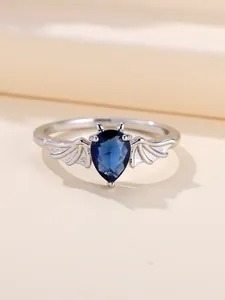 Dettaglio anello a pipistrello con gemma blu a goccia e ali gotiche su metallo argentato