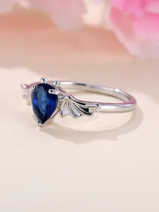 Dettaglio dell'anello con gemma blu a goccia e ali di pipistrello in argento lucido