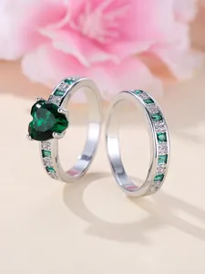 Macro shot of silver stacking rings with heart-shaped emerald stone and crystal accents