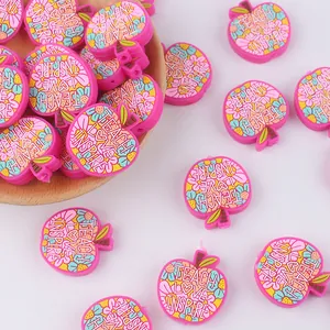 Detalle de cuentas de silicona rosa en forma de manzana con texto Teach Love Inspire en madera