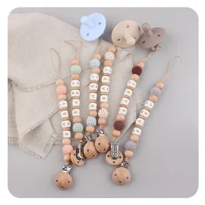 Detail of wooden pacifier clips with silicone beads and crochet balls in Morandi colors