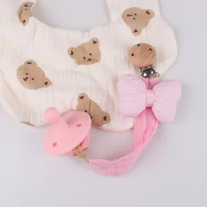 Detailansicht eines Baby-Latzes mit Bärenmuster und rosa Schnullerkette mit Schleife