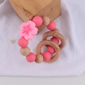 Detail of pink silicone floral teething bracelet with natural beech wood rings on linen