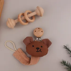Detail of baby pacifier clip with brown plush bear, cotton strap and round wooden clamp