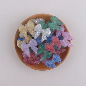 Close-up of glitter bow-shaped silicone beads for DIY pacifier clips on a wood tray
