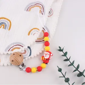 Detail of baby pacifier clip with silicone beads and Santa Claus doll on white fabric