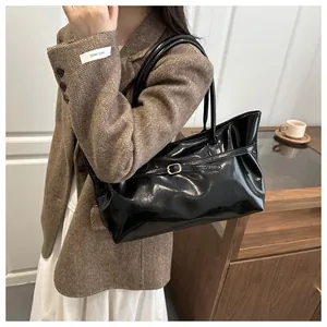 Détail du sac seau en cuir verni noir avec boucle dorée décorative et fines lanières