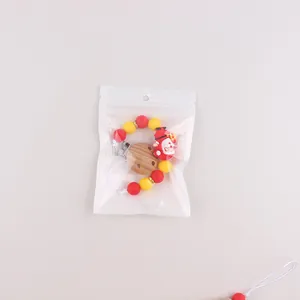 Detail of baby pacifier clip with red Santa silicone beads and wooden clasp in packaging