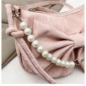 Detail of light pink shoulder bag with large bow and elegant white pearl strap accessory