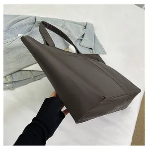 Detail van de grote donkerbruine PU-lederen tote bag op witte doek met denim jasje