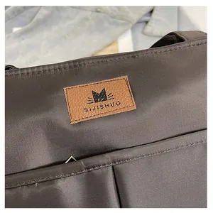 Detail van bruine nylon shopper met SIJISHUO-logopatch en fijne stofstructuur