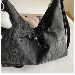 Détail du sac noir plissé avec poche à cordon et charmant pompon blanc moelleux en contraste