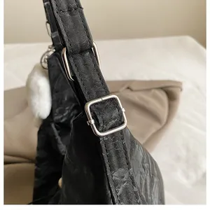 Détail du sac bandoulière plissé noir avec boucle argentée et pompon blanc doux