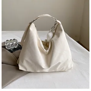 Détail d'un sac à bandoulière beige avec texture souple et pendentif boule en peluche