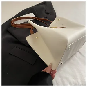 Détail d'un sac cabas crème avec des bandoulières en cuir marron et rivets dorés