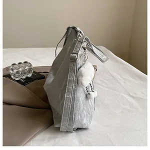 Vue détaillée du sac argenté avec texture plissée et charm en peluche nuage blanc
