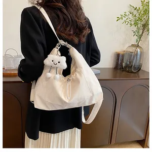 Sac demi-lune beige chic avec breloque nuage en peluche porté à l'épaule