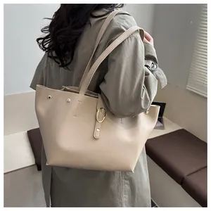 Détail d'un sac cabas beige en cuir avec boucle dorée, porté avec un trench-coat kaki