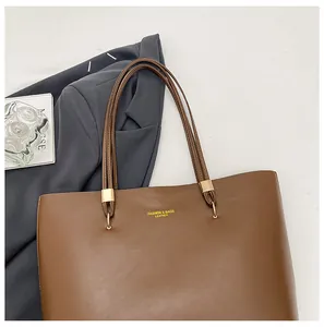 Detail of dark brown leather tote bag with gold metal buckles and thin shoulder straps