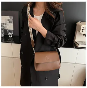 Brown leather crossbody bag with geometric woven strap shown on a model in a trench coat