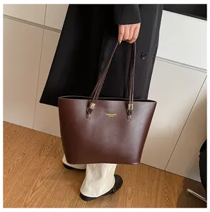 Detail of dark brown leather tote bag showing gold logo and thin shoulder straps